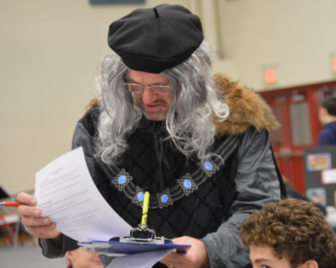 Mr. Willis goes over a student's project dressed in Renaissance attire from head to toe. He wore a fur-lined grey and black tunic accessorized with a grey wig on his head and black tights on his legs.