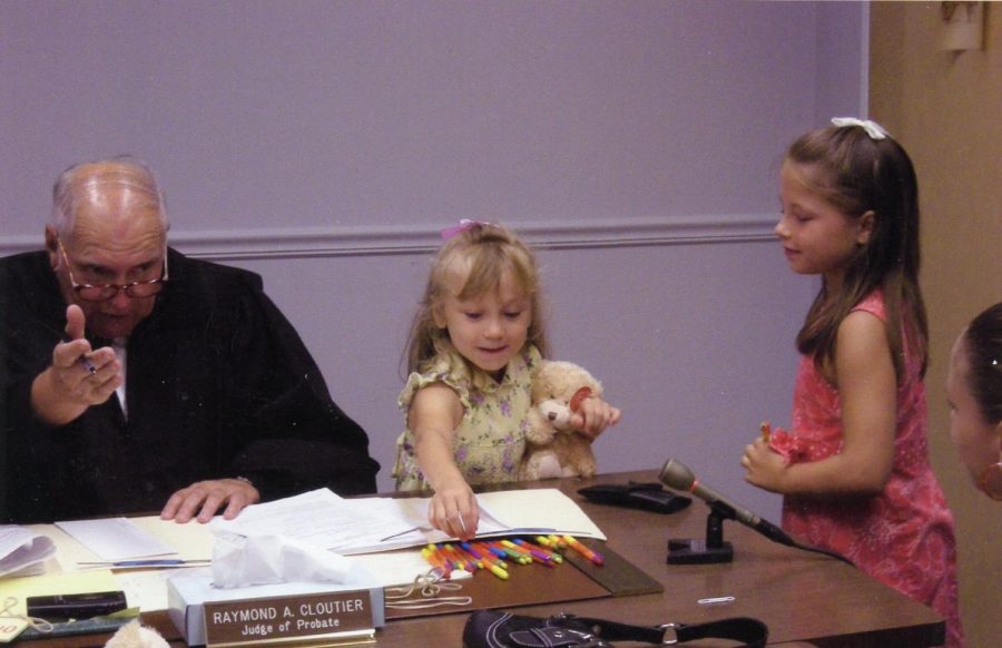 Alyssa and Marissa Neal sit with a judge and sign various documents at their adoption hearing.
