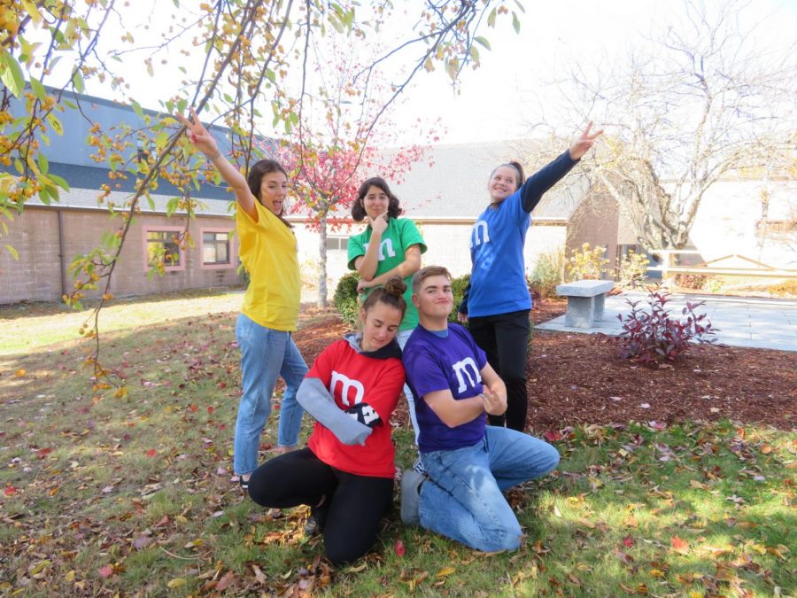 Junior Isabella McCutcheon (yellow), senior Jillian Morani (green), sophomore Laura Haas (blue), senior Kait Bedell (red), and senior Sean Cavanaugh (purple) get into the wacky spirit of their collaborated costumes. Each of their shirts cost $3 to produce, making the combined total for the entire ensemble $15.