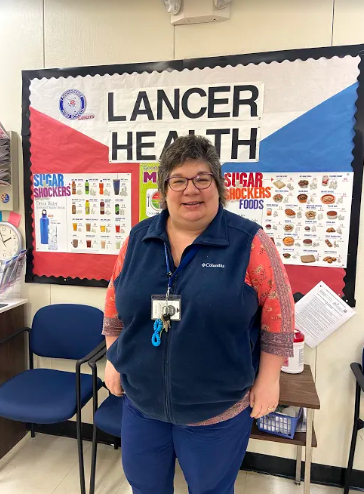 LHS Nurse Mrs. Cullen stands in front of Lancer Health bulletin board in the school nurse office. 