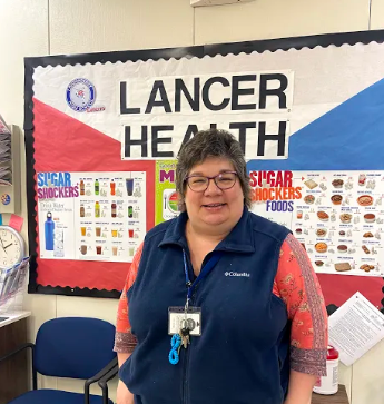 LHS Nurse Mrs. Cullen stands in front of "Lancer Health" bulletin board in the school nurse office.