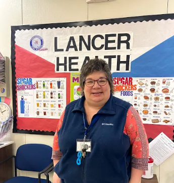 LHS Nurse Mrs. Cullen stands in front of Lancer Health bulletin board in the school nurse office. 