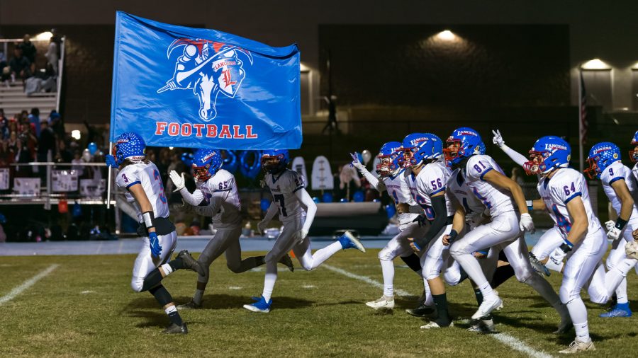 Varsity football runs onto the field proudly waving their flag before the game begins.