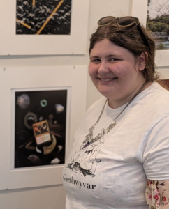Senior Caitlyn Muller beside her art at a gallery at New England College. Muller is also pictured wearing a shirt with her own artwork.

Photo provided by Caitlyn Muller