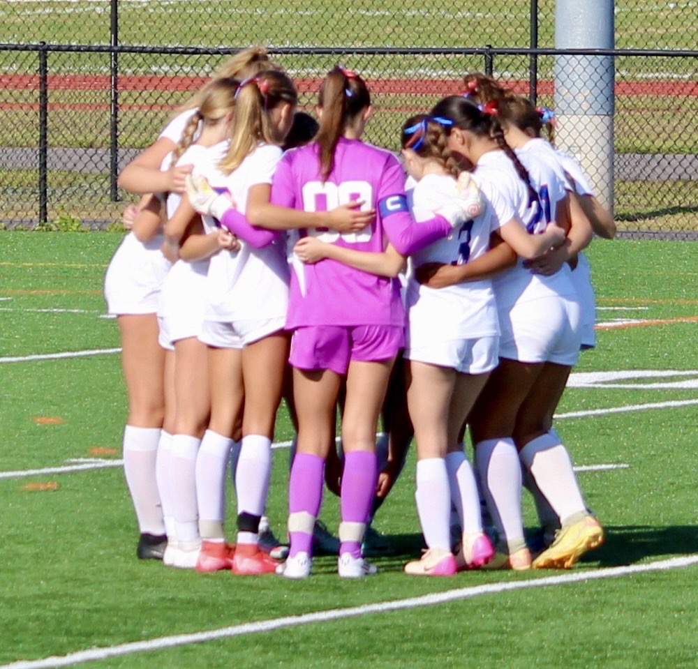 The girls' soccer team huddles up, focusing on teamwork and strategy.