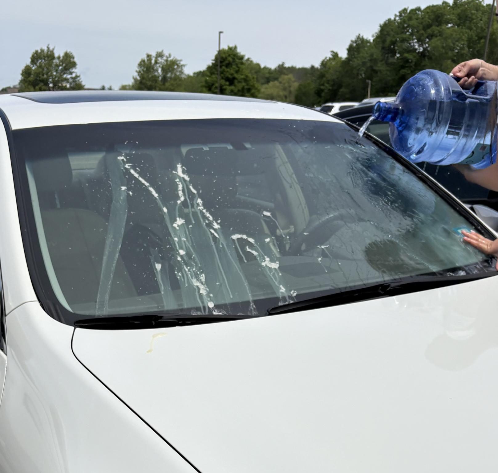 Junior Lillian Barud uses a jug of water to clear the whipped cream off her car’s windshield in the main lot. Like Barud, many of the students who found their cars covered in whipped cream were forced to wash it off themselves.
(Photo used with permission by Mia Robinson)