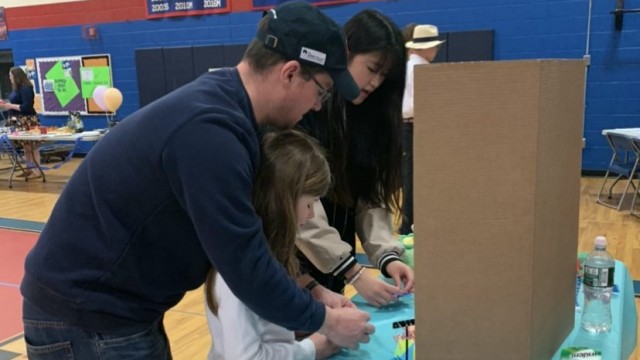 Aika Chen instructs Reece Sutherland on how to make the traditional Japanese origami crane with the help of Reece's father, David Sutherland.
